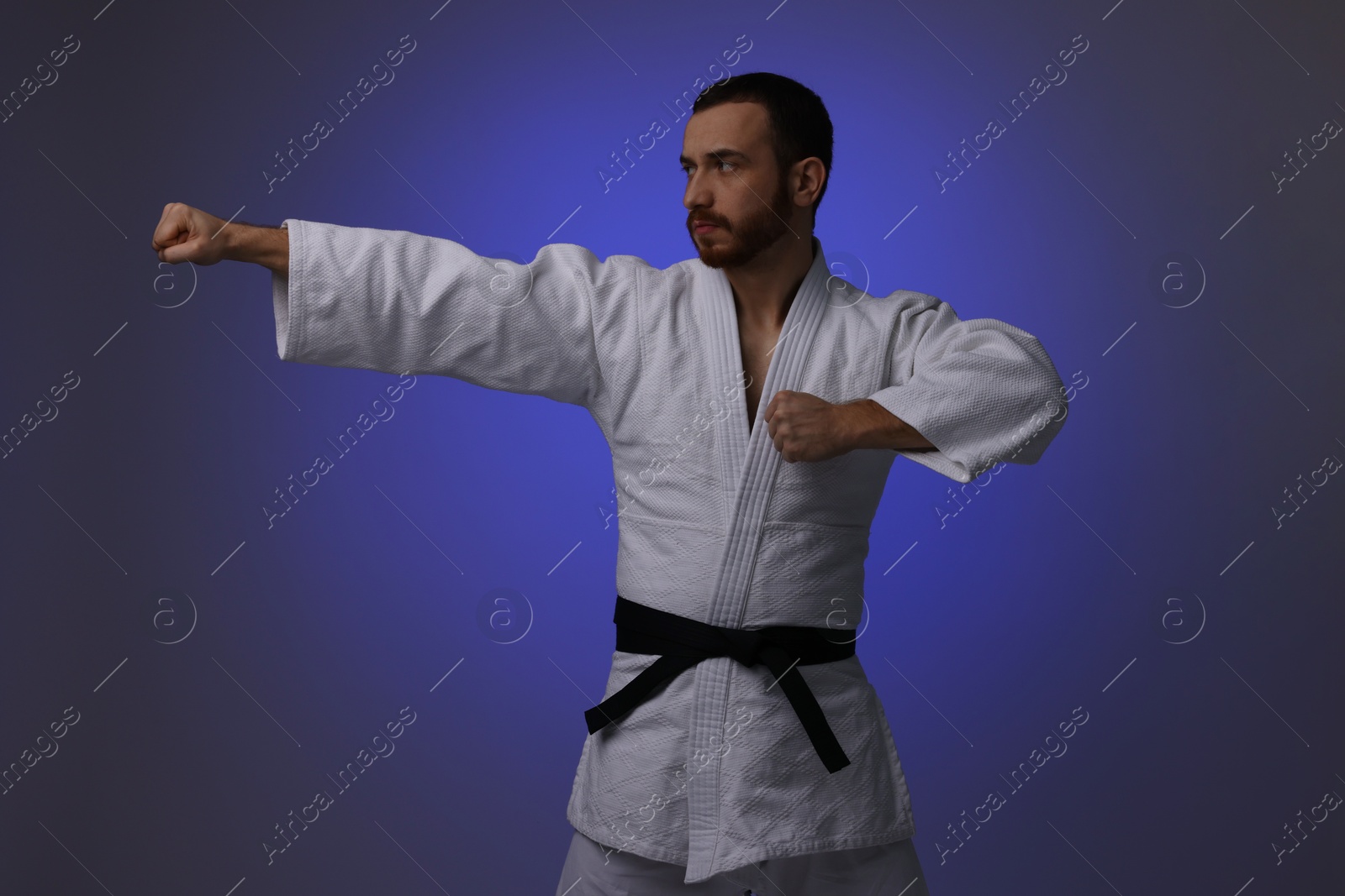 Photo of Man in uniform practicing karate on dark purple background