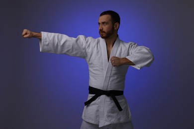 Photo of Man in uniform practicing karate on dark purple background