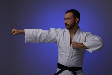 Photo of Man in uniform practicing karate on dark purple background