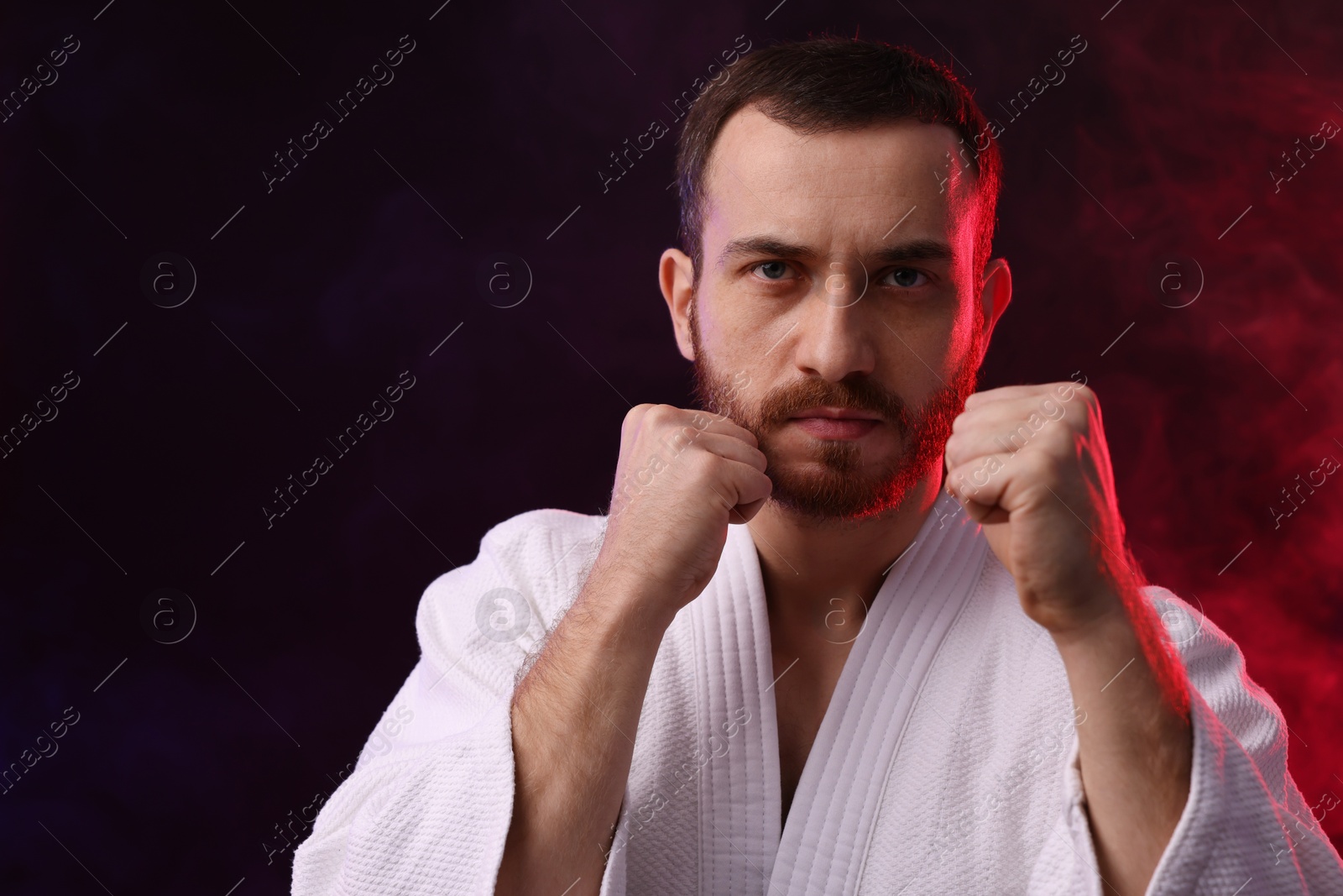 Photo of Karate fighter in color lights and smoke against black background. Space for text