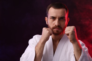 Photo of Karate fighter in color lights and smoke against black background. Space for text