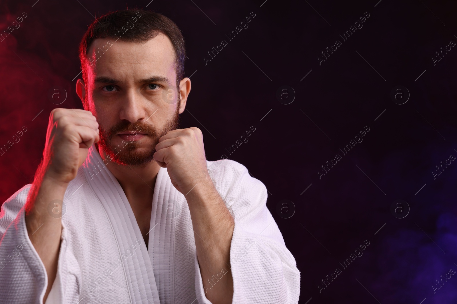 Photo of Karate fighter in color lights and smoke against black background. Space for text