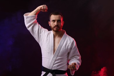 Photo of Man wearing uniform practicing karate in color lights and smoke against black background