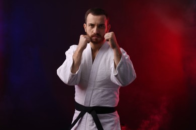 Photo of Man wearing uniform practicing karate in color lights and smoke