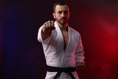 Photo of Man wearing uniform practicing karate in color lights and smoke