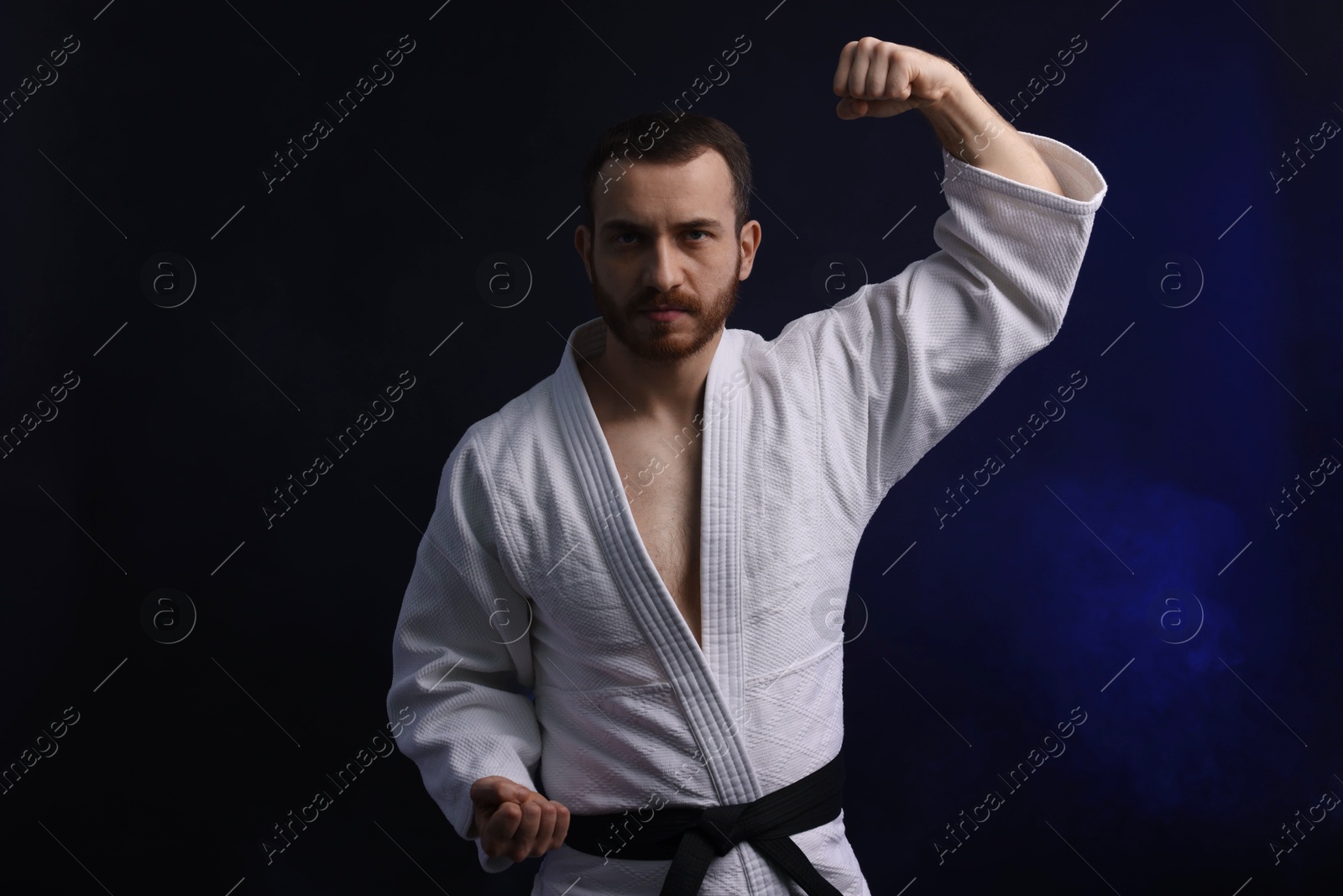 Photo of Man in uniform practicing karate on dark background