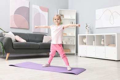 Photo of Little girl exercising on fitness mat at home. Sport activity