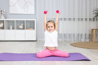 Photo of Little girl exercising with dumbbells on fitness mat at home. Sport activity