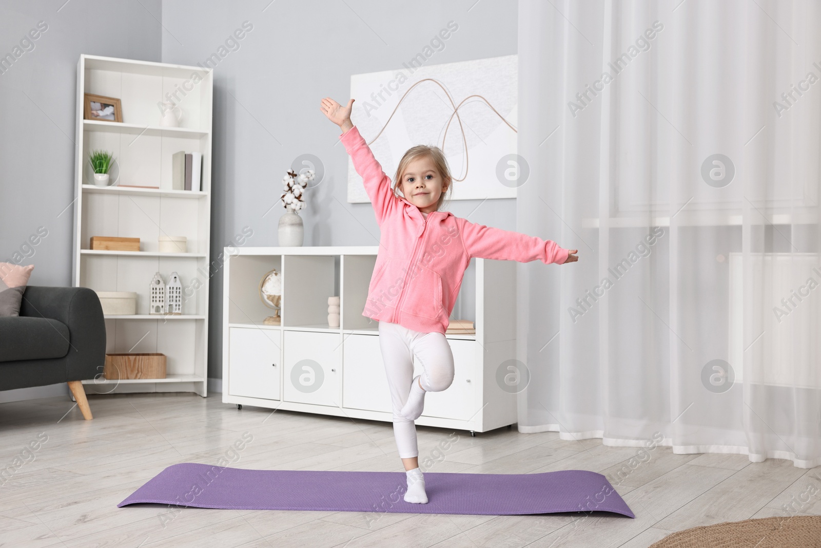 Photo of Little girl exercising on fitness mat at home. Sport activity