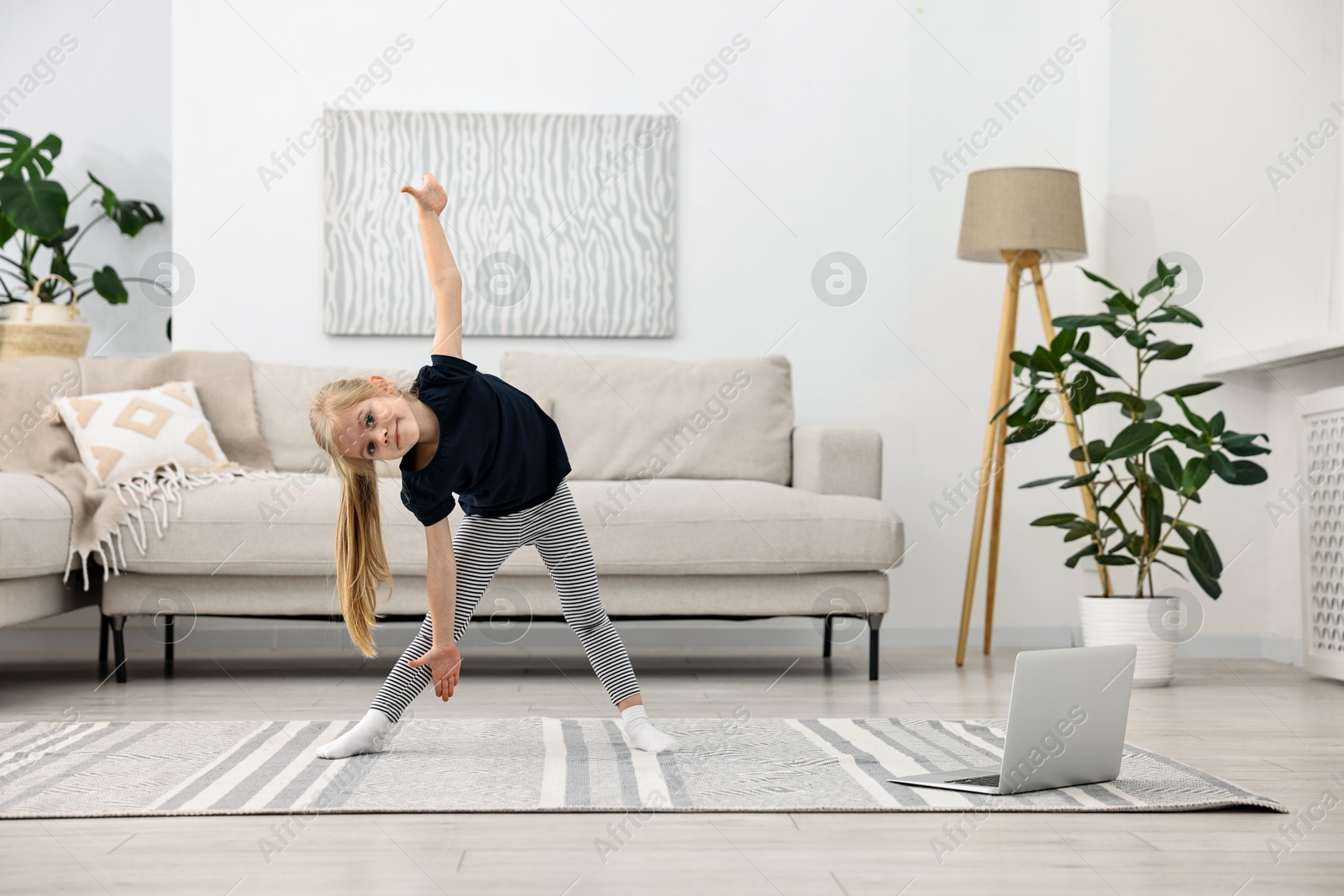 Photo of Little girl exercising with online coach via laptop at home. Sport activity