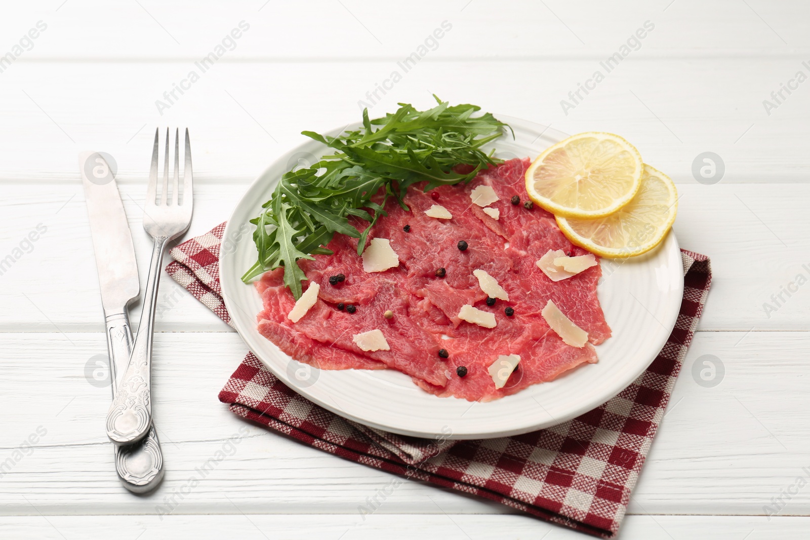 Photo of Fresh beef carpaccio with arugula, lemon and cheese on white wooden table, closeup