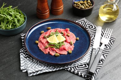 Photo of Fresh beef carpaccio with arugula, lemon and capers on dark textured table