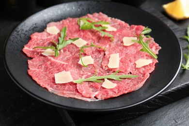 Fresh beef carpaccio with arugula and cheese on dark textured table, closeup