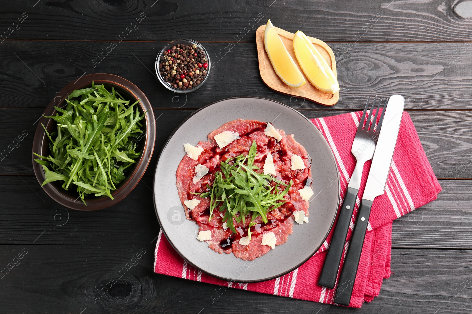 Photo of Fresh beef carpaccio with arugula, cheese and sauce served on black wooden table, flat lay