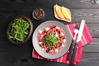 Fresh beef carpaccio with arugula, cheese and sauce served on black wooden table, flat lay