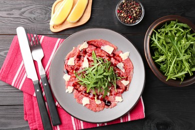 Photo of Fresh beef carpaccio with arugula, cheese and sauce served on black wooden table, flat lay