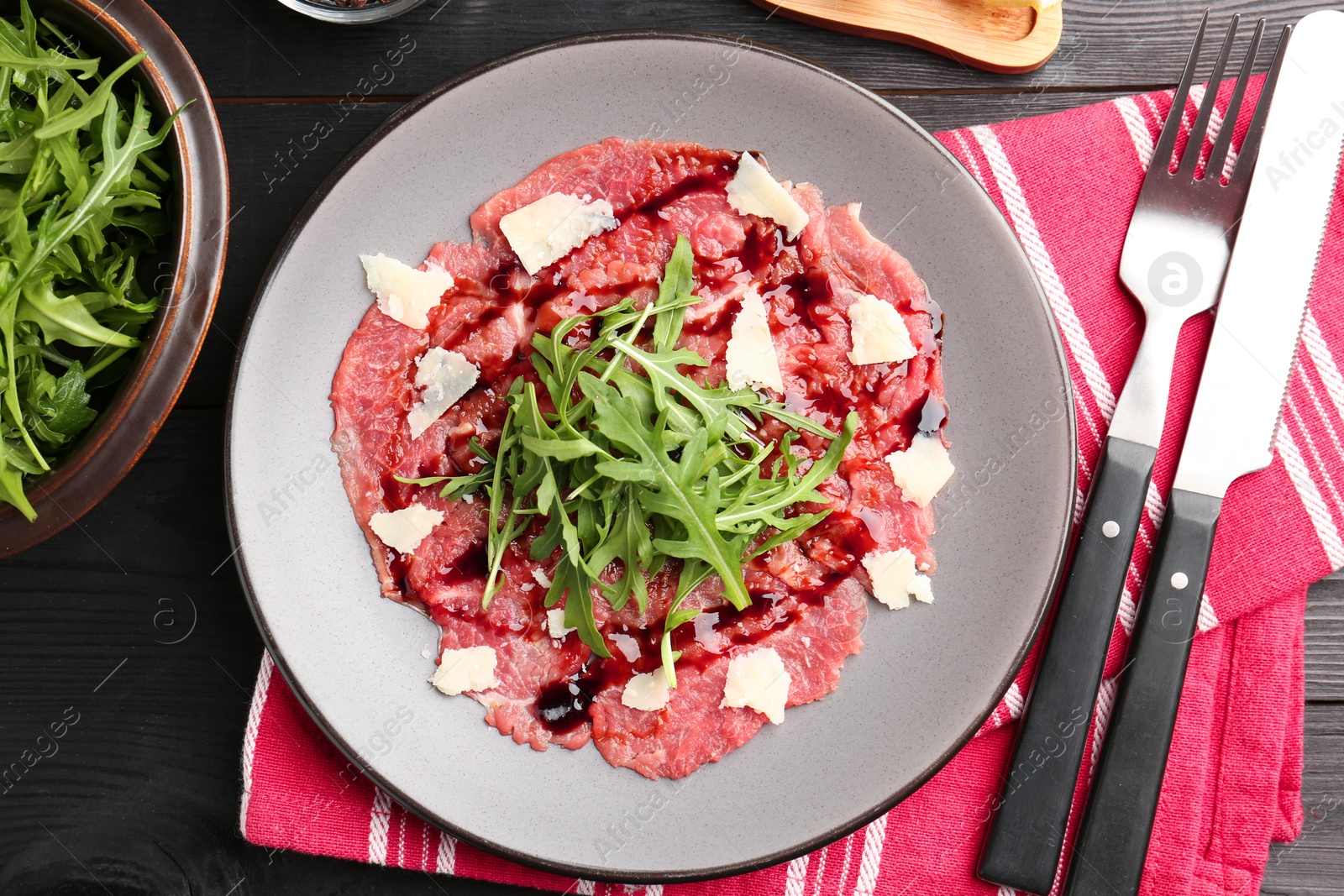 Photo of Fresh beef carpaccio with arugula, cheese and sauce served on black wooden table, flat lay