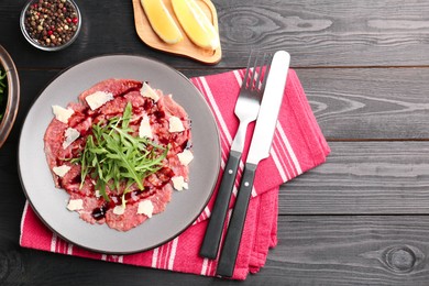 Photo of Fresh beef carpaccio with arugula, cheese and sauce served on black wooden table, flat lay. Space for text