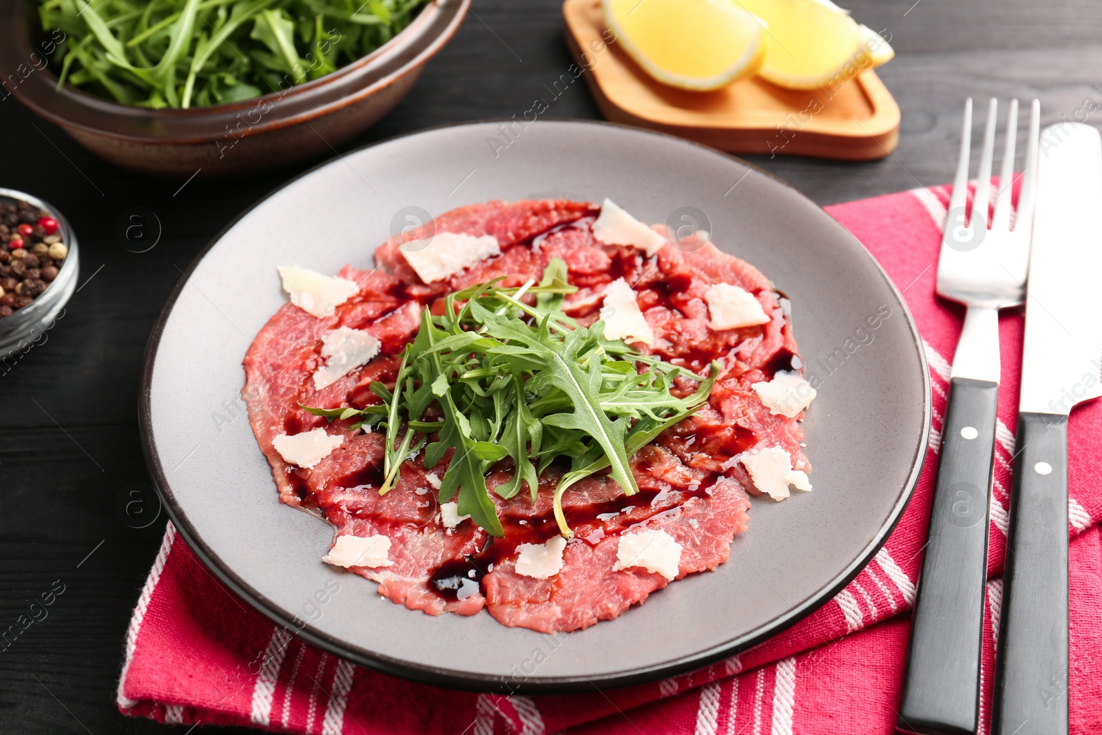 Photo of Fresh beef carpaccio with arugula, cheese and sauce on black wooden table, closeup