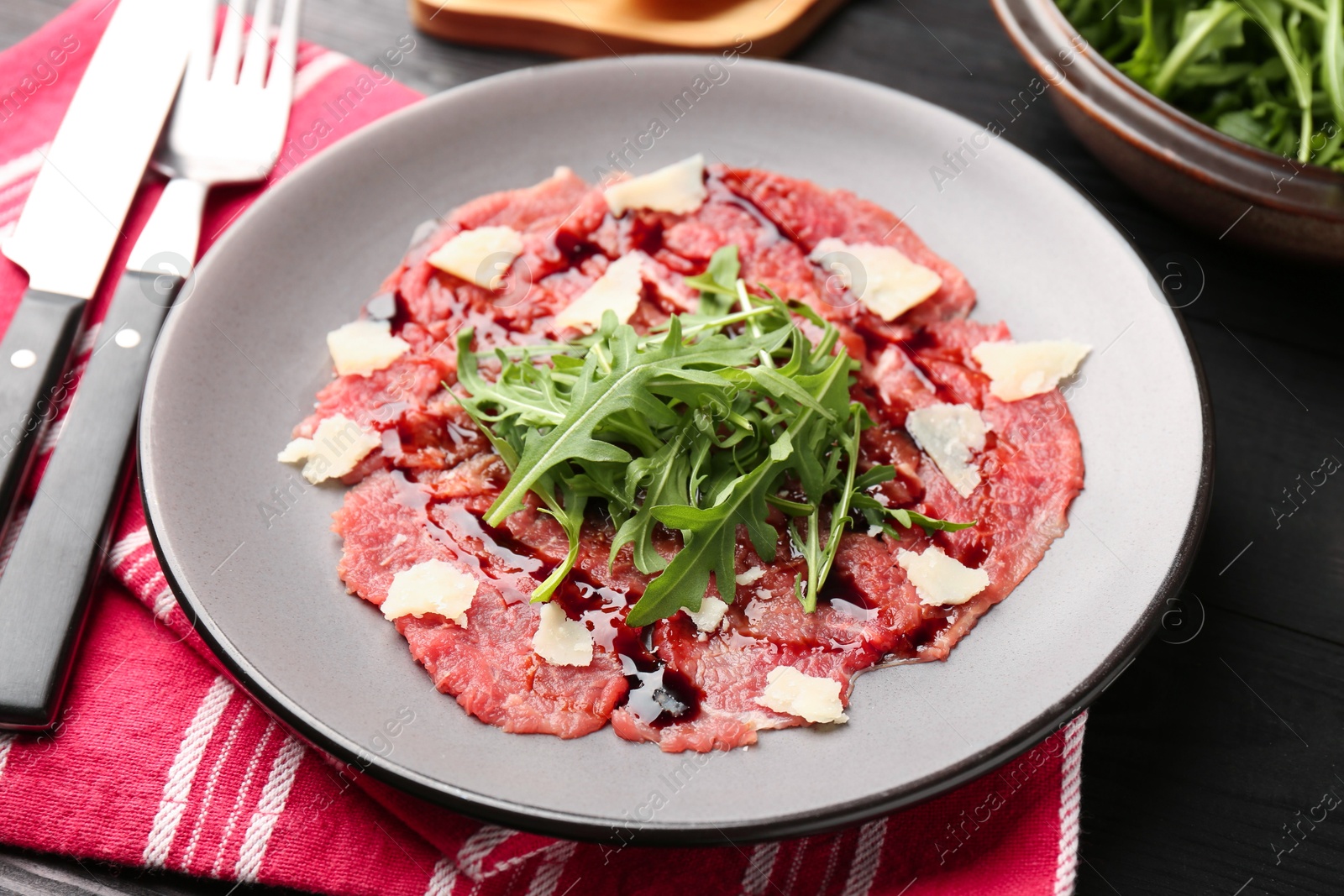 Photo of Fresh beef carpaccio with arugula, cheese and sauce on black table, closeup