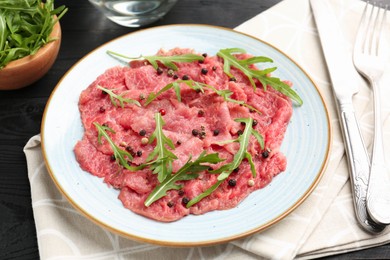 Fresh beef carpaccio with arugula and peppercorns on black wooden table, closeup