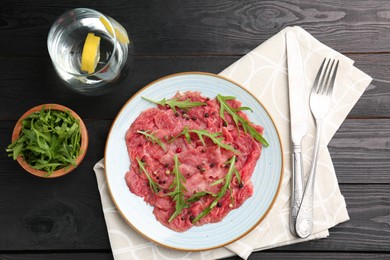 Fresh beef carpaccio with arugula and peppercorns served on black wooden table, flat lay