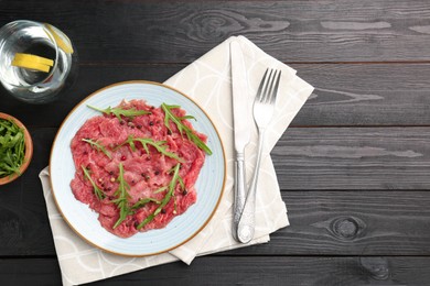 Photo of Fresh beef carpaccio with arugula and peppercorns served on black wooden table, flat lay. Space for text