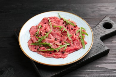 Fresh beef carpaccio with arugula and peppercorns on black wooden table, closeup