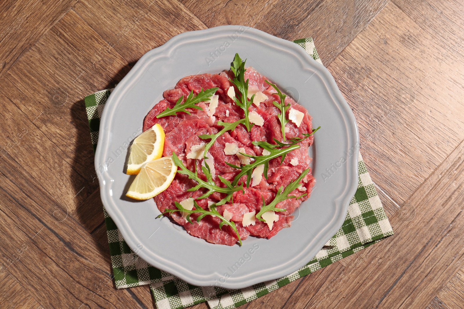 Photo of Fresh beef carpaccio with arugula, cheese and lemon on wooden table, top view