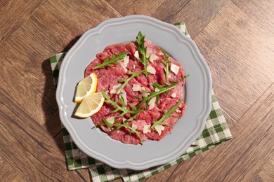 Fresh beef carpaccio with arugula, cheese and lemon on wooden table, top view