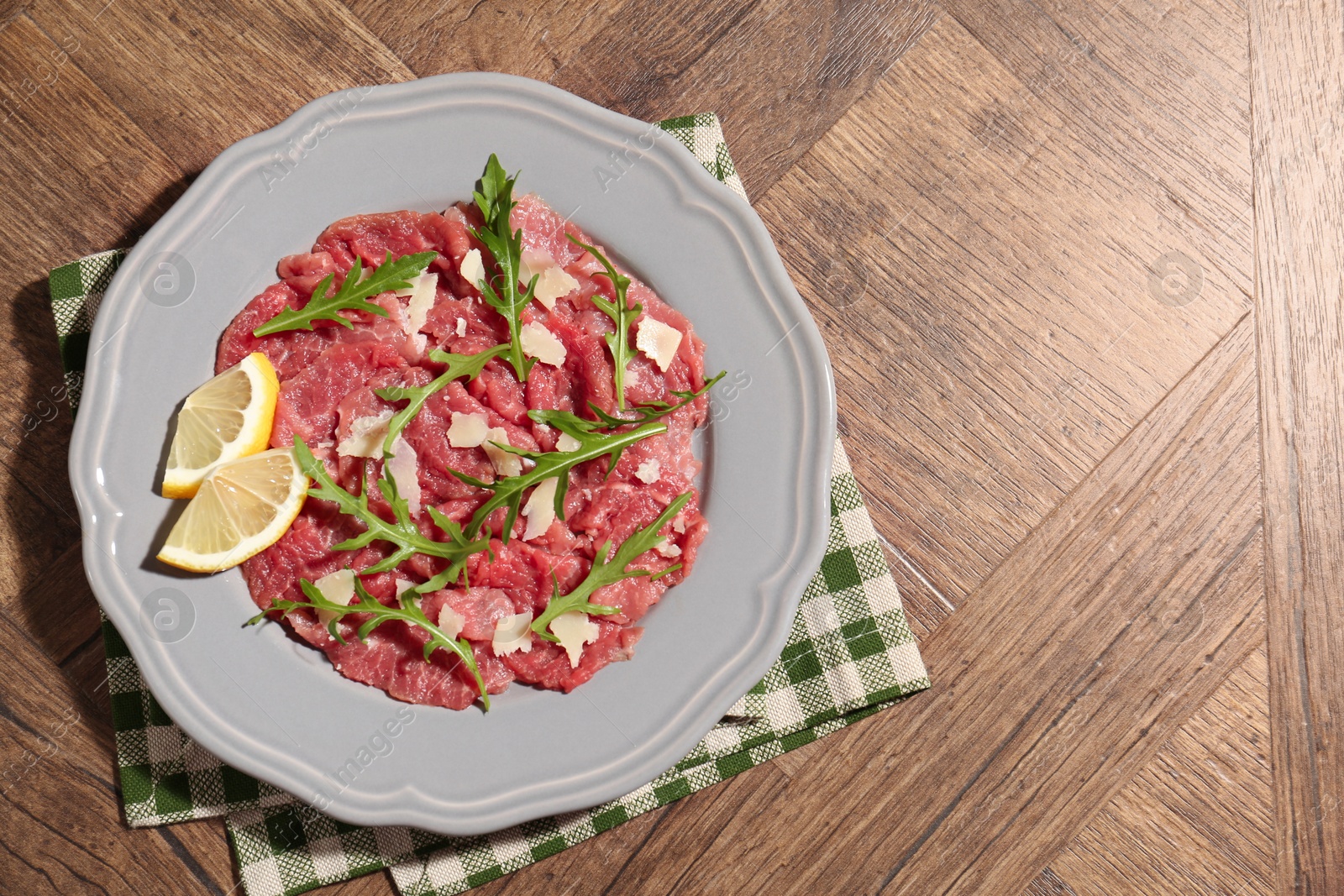 Photo of Fresh beef carpaccio with arugula, cheese and lemon on wooden table, top view. Space for text