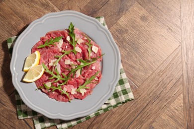 Photo of Fresh beef carpaccio with arugula, cheese and lemon on wooden table, top view. Space for text