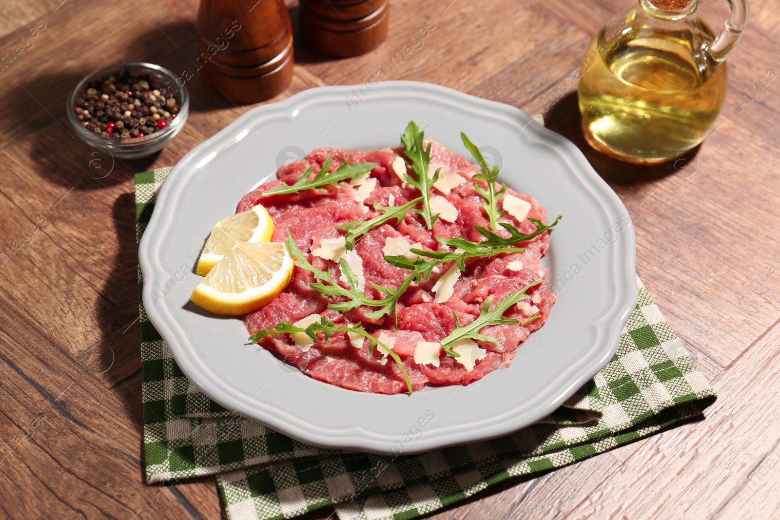 Photo of Fresh beef carpaccio with arugula, cheese and lemon on wooden table, closeup