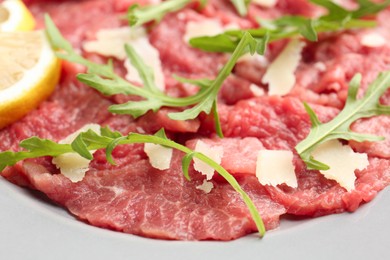 Fresh beef carpaccio with arugula, cheese and lemon on plate, closeup