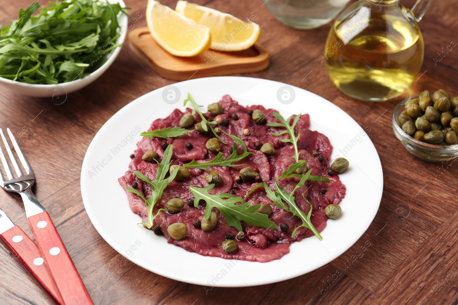 Photo of Fresh beef carpaccio with arugula and capers on wooden table, closeup