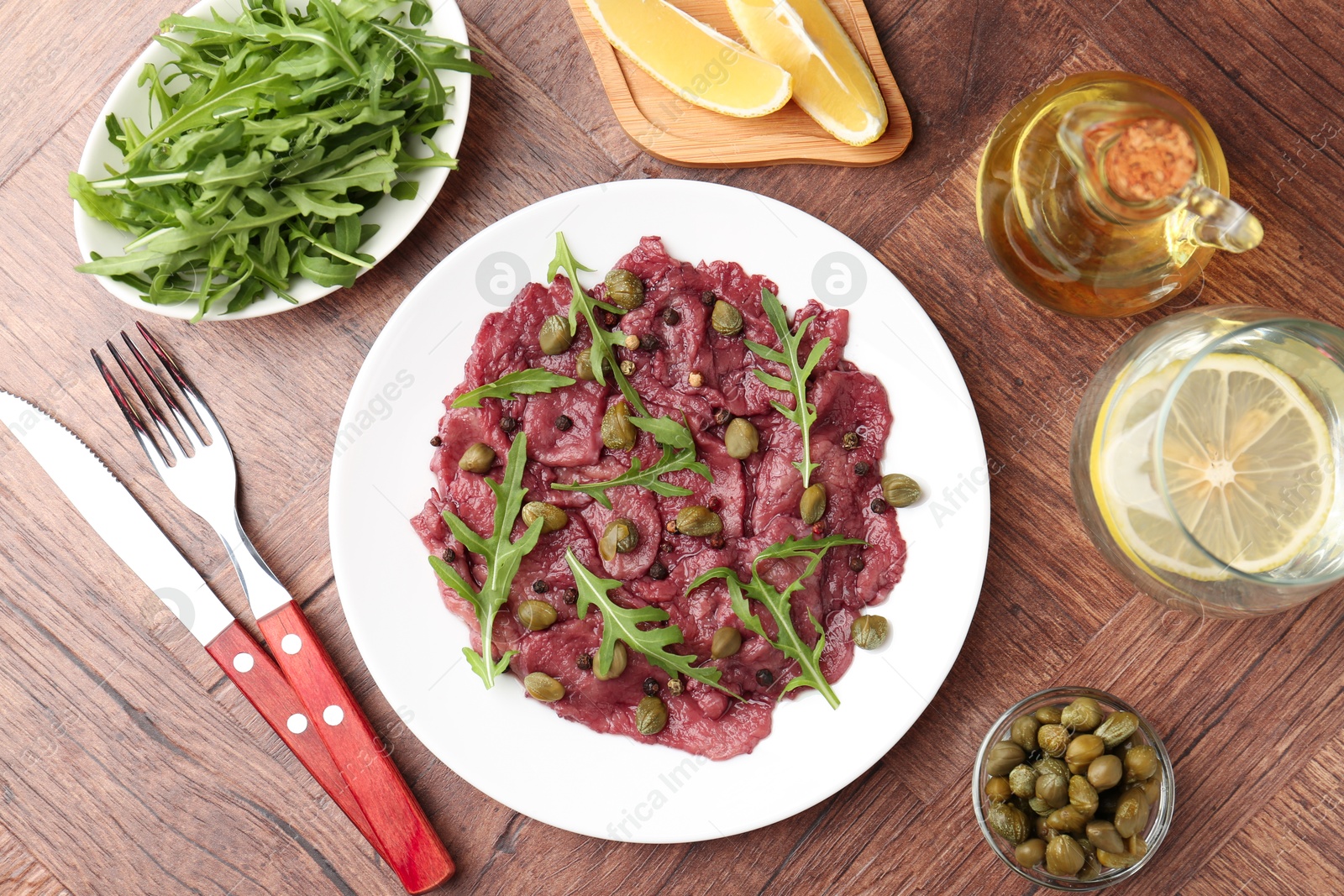 Photo of Fresh beef carpaccio with arugula and capers served on wooden table, flat lay