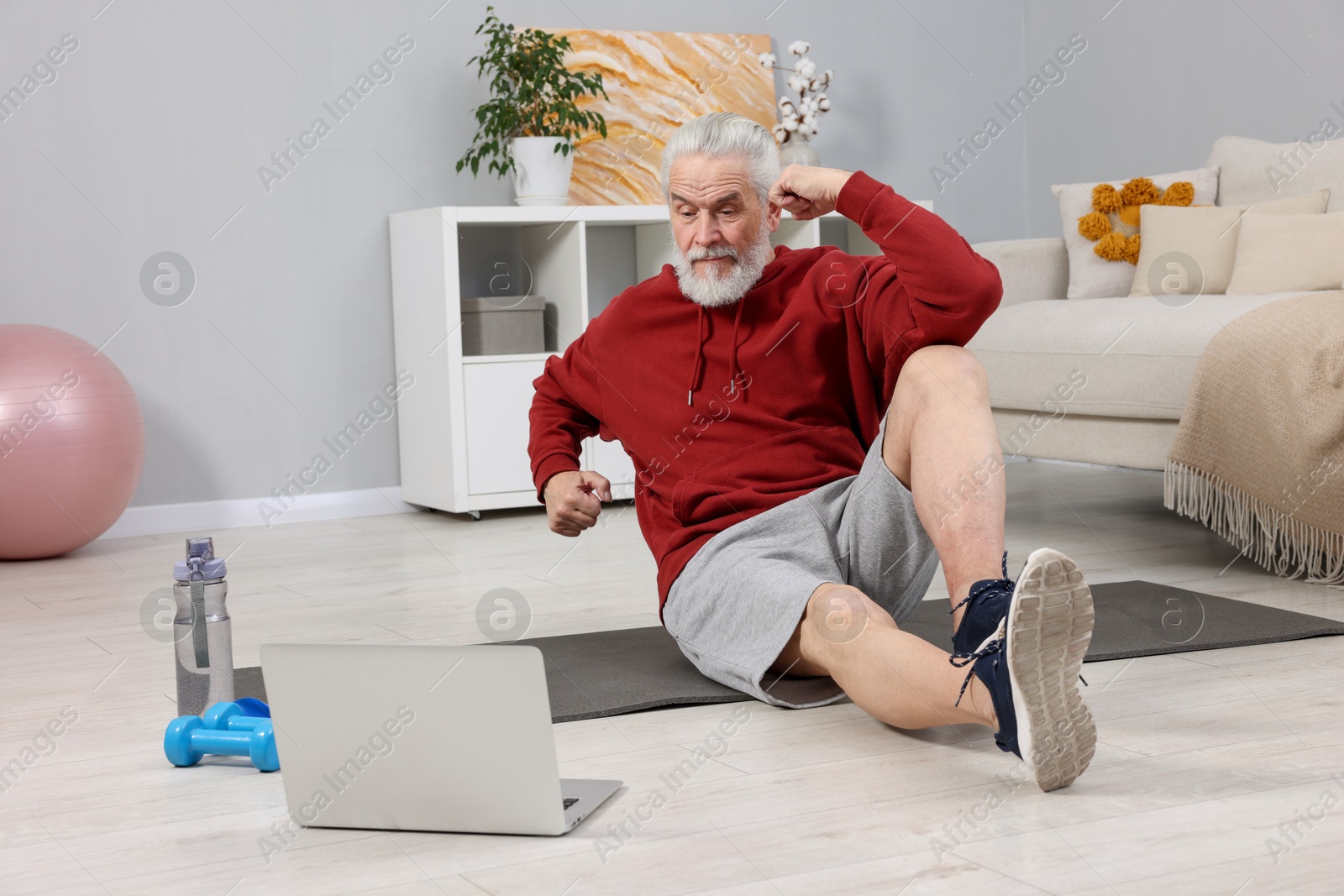 Photo of Elderly man exercising near laptop at home