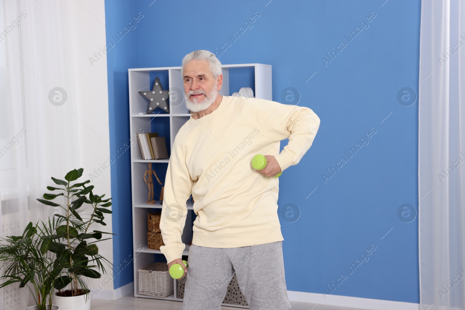 Photo of Elderly man exercising with dumbbells at home