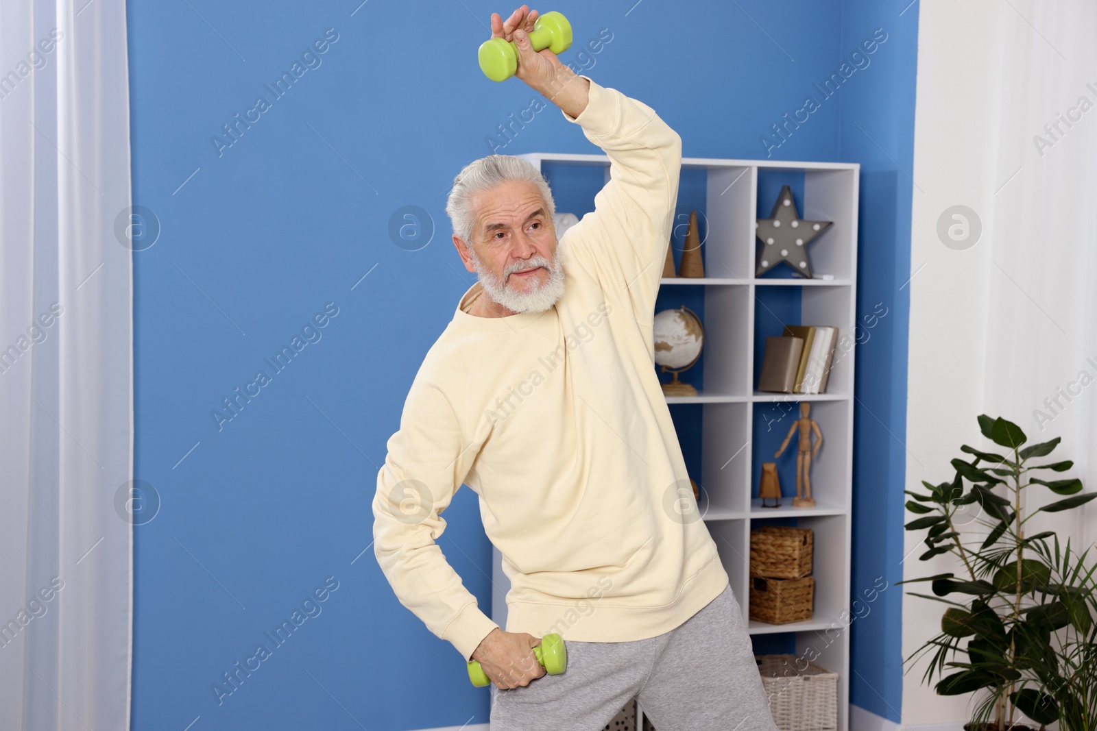 Photo of Elderly man exercising with dumbbells at home