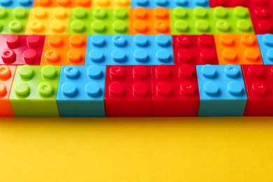 Photo of Constructor toy. Many colorful building blocks on yellow background, closeup. Space for text