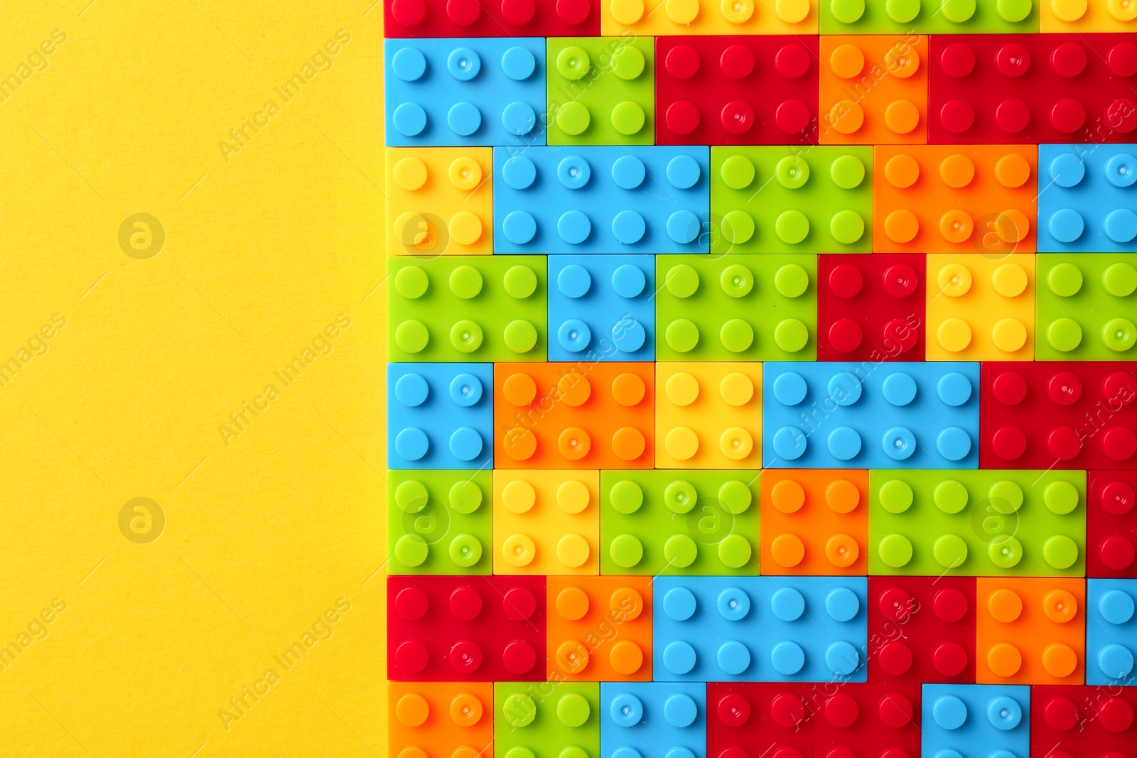 Photo of Constructor toy. Many colorful building blocks on yellow background, top view. Space for text