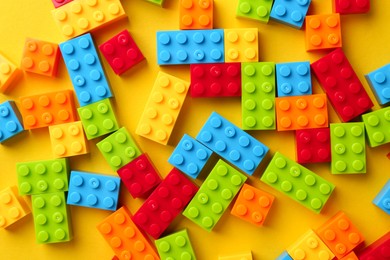 Photo of Constructor toy. Many colorful building blocks on yellow background, flat lay