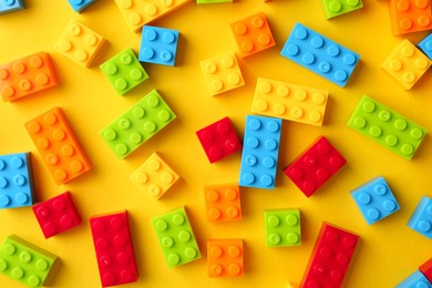 Photo of Constructor toy. Many colorful building blocks on yellow background, flat lay