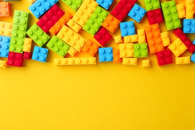 Photo of Constructor toy. Many colorful building blocks on yellow background, flat lay. Space for text