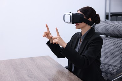 Photo of Woman using virtual reality headset in office, space for text