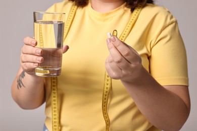 Photo of Plus size woman with weight loss supplements and glass of water on grey background, closeup