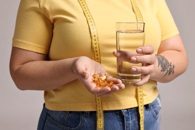 Photo of Plus size woman with weight loss supplements and glass of water on grey background, closeup