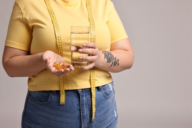 Photo of Plus size woman with weight loss supplements and glass of water on grey background, closeup. Space for text