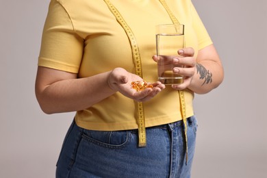 Photo of Plus size woman with weight loss supplements and glass of water on grey background, closeup