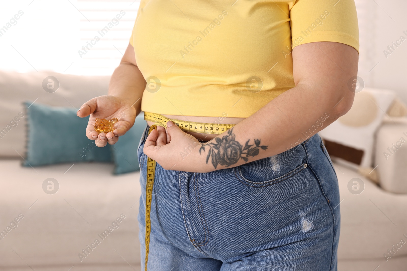 Photo of Plus size woman measuring waist with tape and holding pile of weight loss supplements at home, closeup